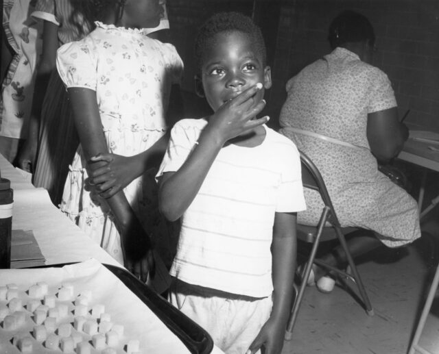 Black-and-white photo showing an African American boy taking an oral polio vaccine.